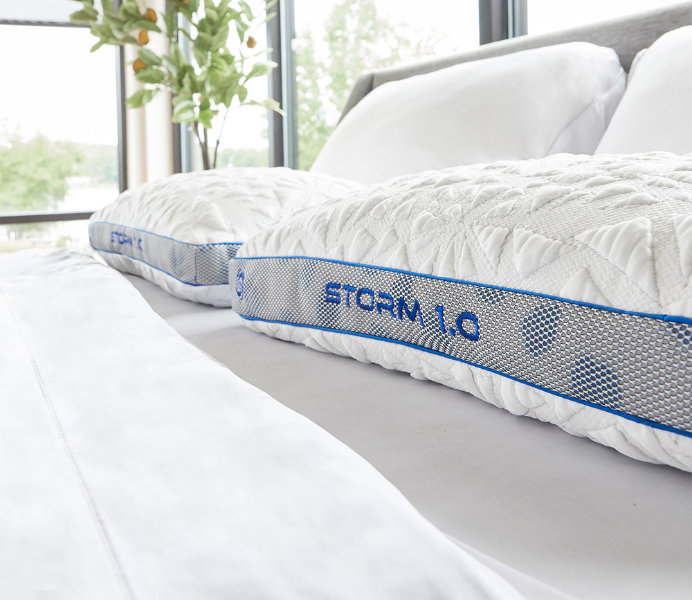 White pillows with 'STORM 1.0' branding on a bed in a bright room with plants.