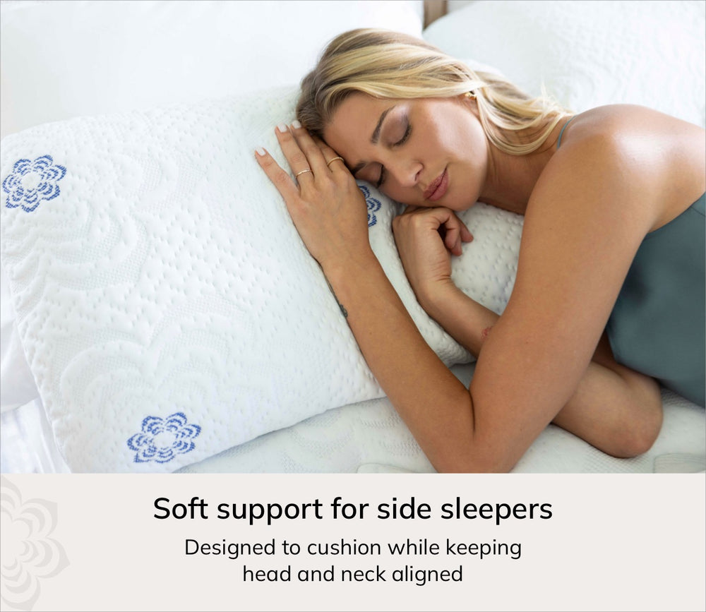 A woman sleeping on her side rests her head on a white quilted pillow with blue floral embroidery, with text below reading 'Soft support for side sleepers' and 'Designed to cushion while keeping head and neck aligned'.