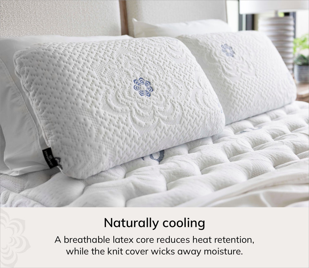 Two white textured pillows with blue embroidered floral details resting on a white quilted mattress, with text below reading 'Naturally cooling' and a descriptive blurb about breathable latex and moisture wicking.
