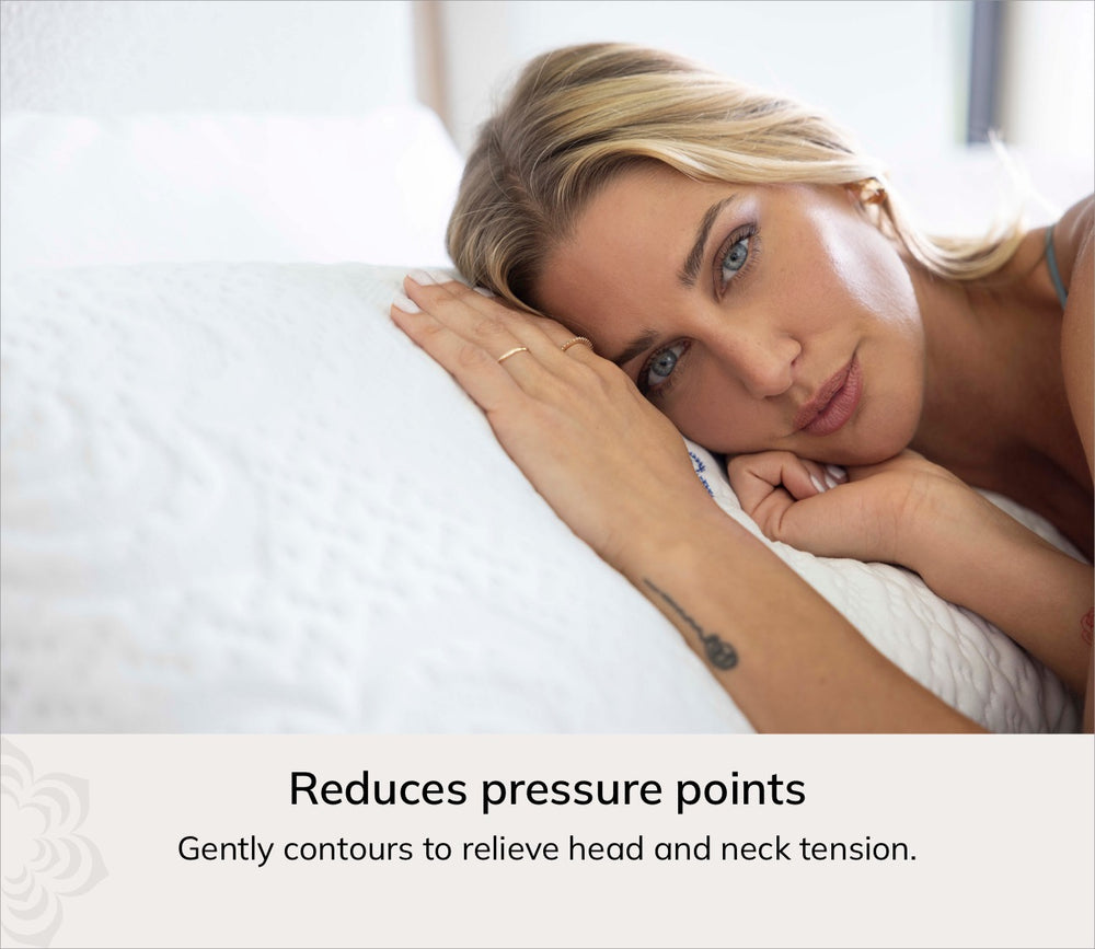 A woman resting her head on a white quilted pillow in a softly lit bedroom, with text at the bottom stating it reduces pressure points and relieves head and neck tension.