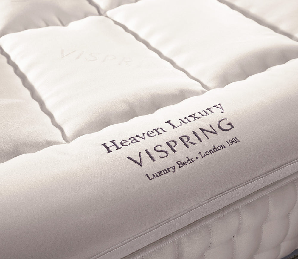 Close-up of Heaven luxury mattress topper with visible branding text reading 'Heaven Luxury VISPRING' and smaller text 'Luxury Beds • London 1901'.