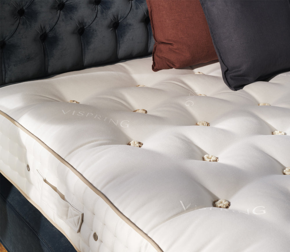A close-up top view of Tiara Superb Mattress set against a dark tufted headboard with decorative pillows.