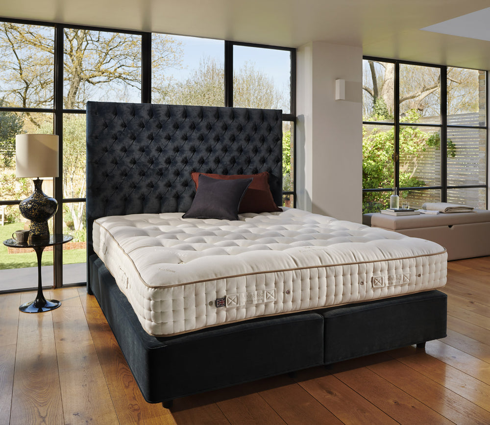 Tiara Superb mattress on a dark tufted box spring bed in a modern bedroom with large windows, hardwood floors, and a side table with a lamp.