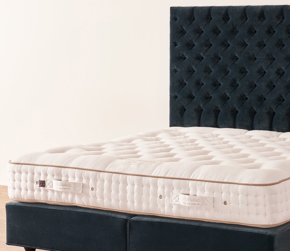 Close-up of Tiara Superb mattress on a dark navy tufted bed frame against a plain off-white wall.
