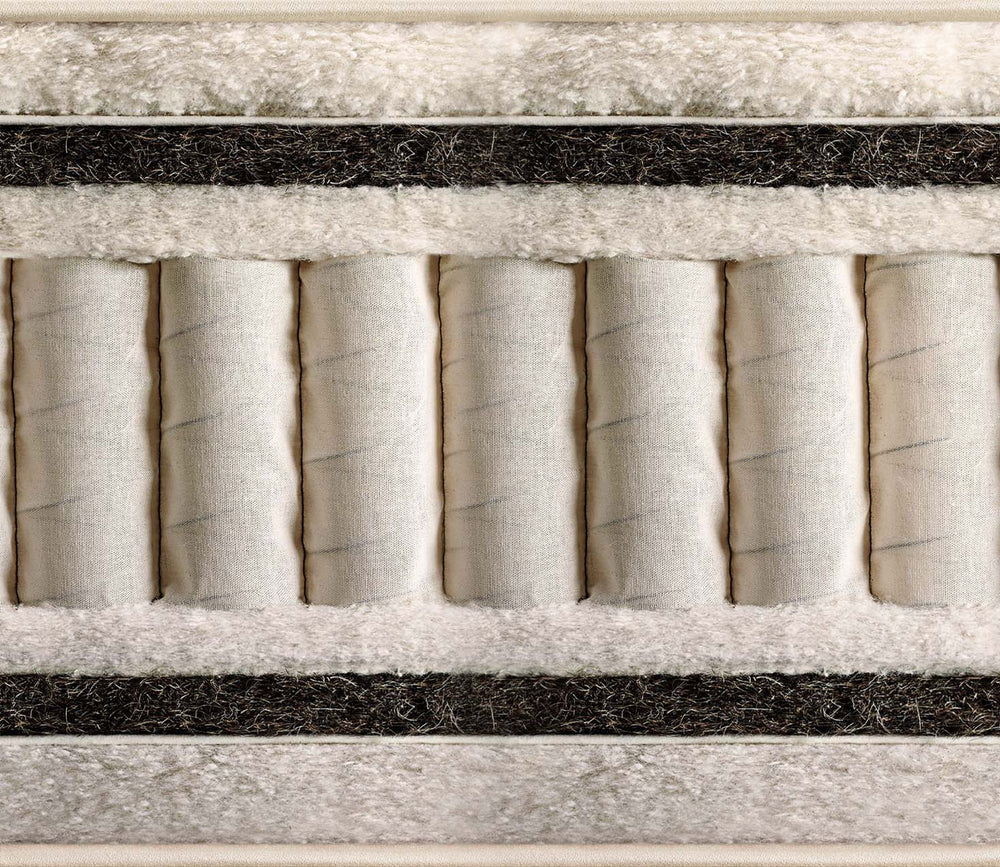 Close-up of the layers of Vispring Herald Superba mattress   showing off-white cylindrical inserts, white plush padding, and dark charcoal horizontal bands.