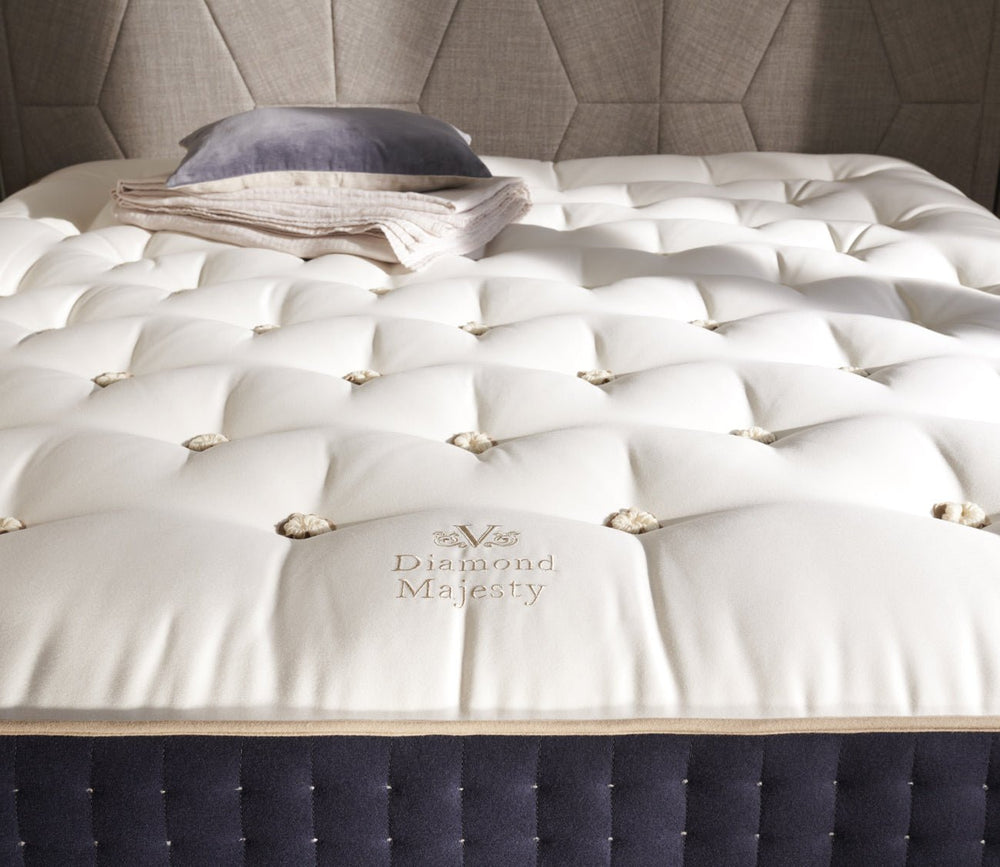 Detailed view of the Vispring Diamond Majesty mattress with a plush hand-tufted top, embroidered logo, and folded blanket and pillow.