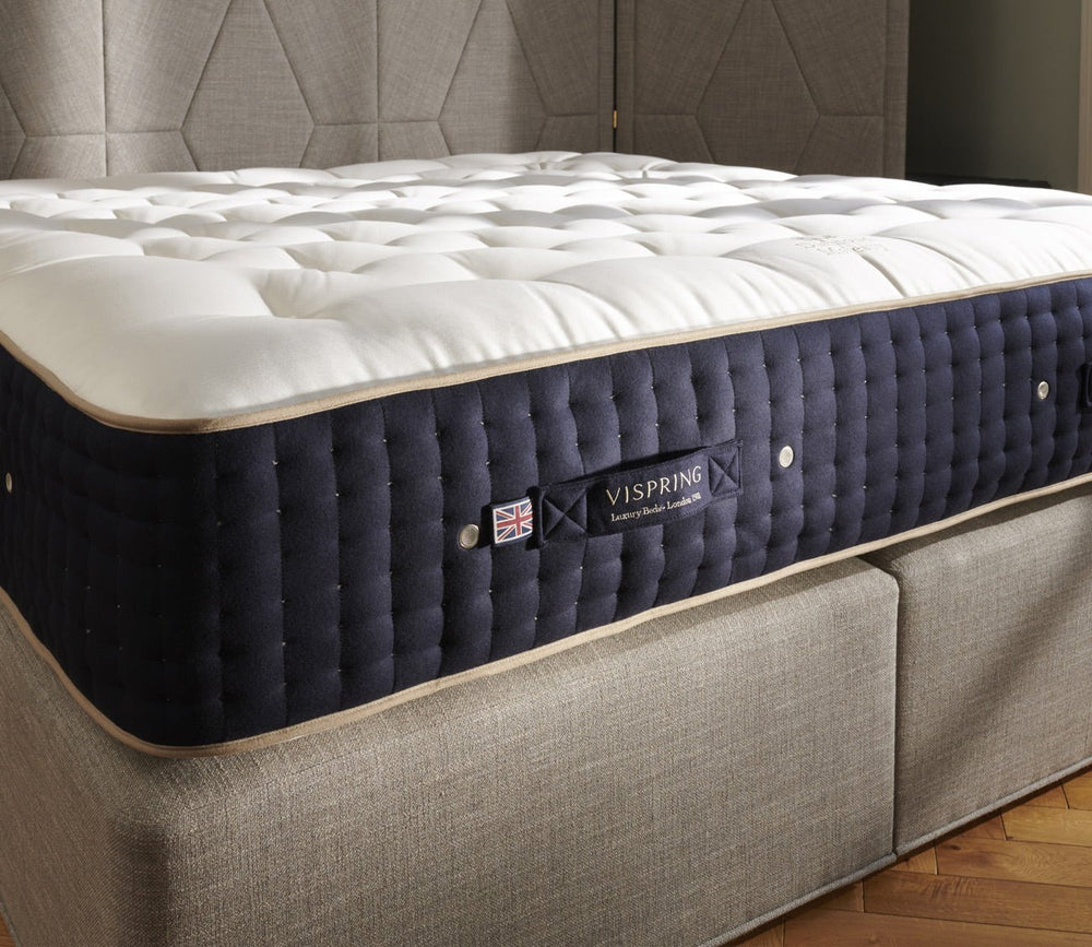 Angled view of a Vispring mattress featuring a plush hand-tufted top, navy side panels, and coordinating upholstered base.