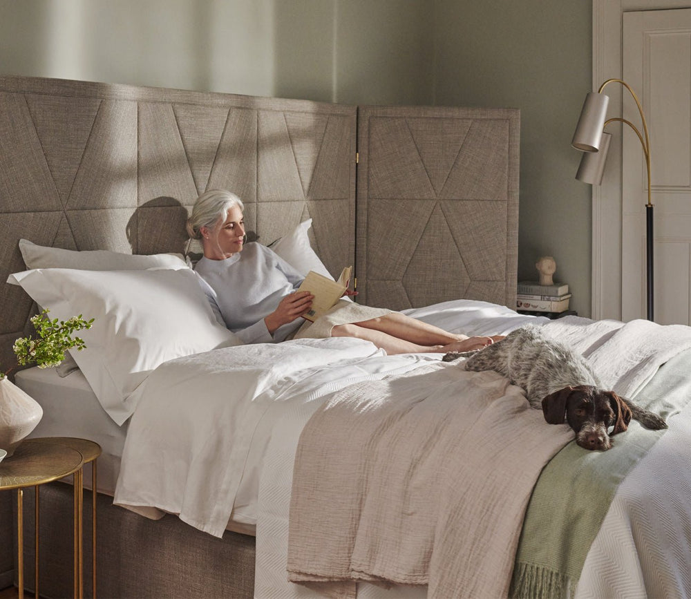 A woman reading a book on a Vispring Diamond Majesty Mattress in a lifestyle setting
