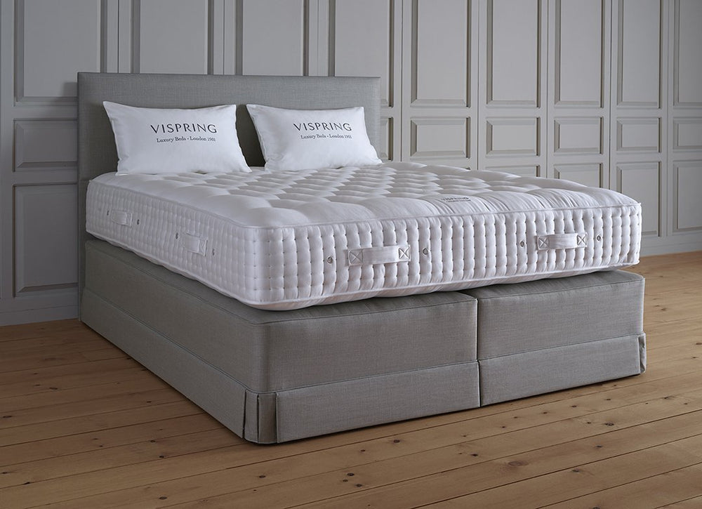 Vispring Masterpiece Superb Plush Mattress featuring a hand-tufted white sleep surface on a gray upholstered divan base with matching headboard.